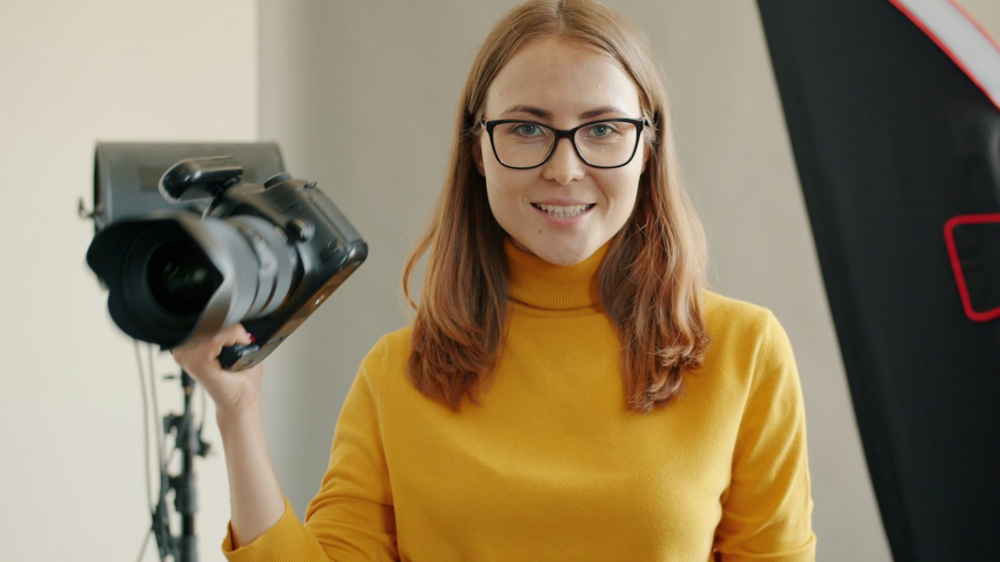 Kobieta w żółtym swetrze trzymająca profesjonalny aparat fotograficzny.